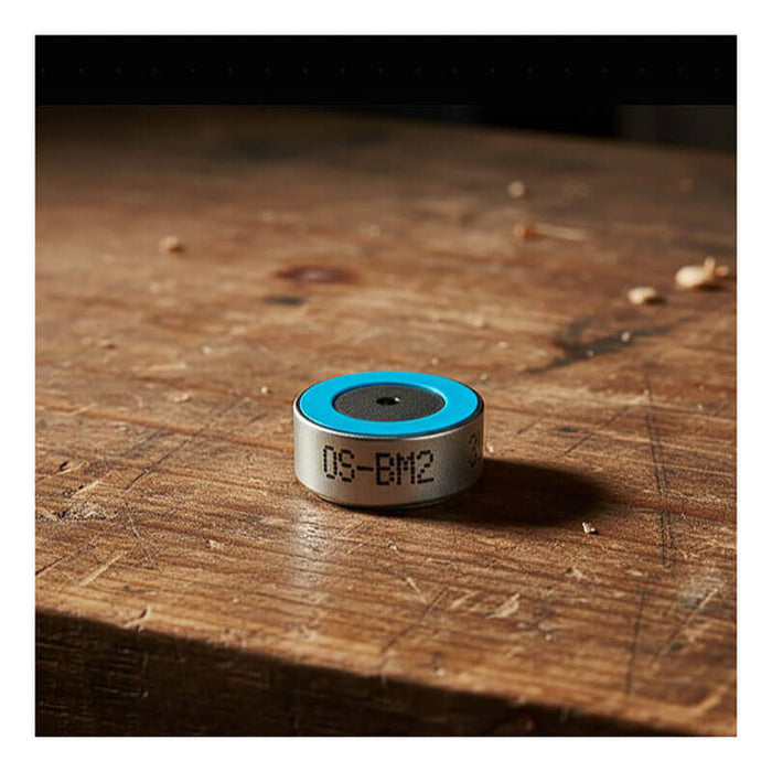A small, round metal object with a blue top, labeled "OS-BM2," sits on a wooden surface amid wood shavings—a RKI Instruments replacement oxygen sensor compatible with the GX-6000 gas monitor.